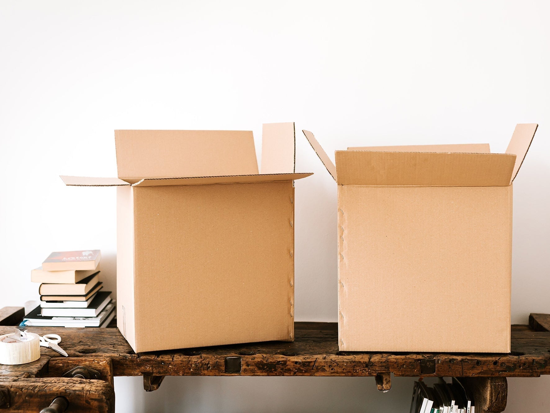 Moving boxes sitting on a wood table with a small stack of books, packing tape and scissors