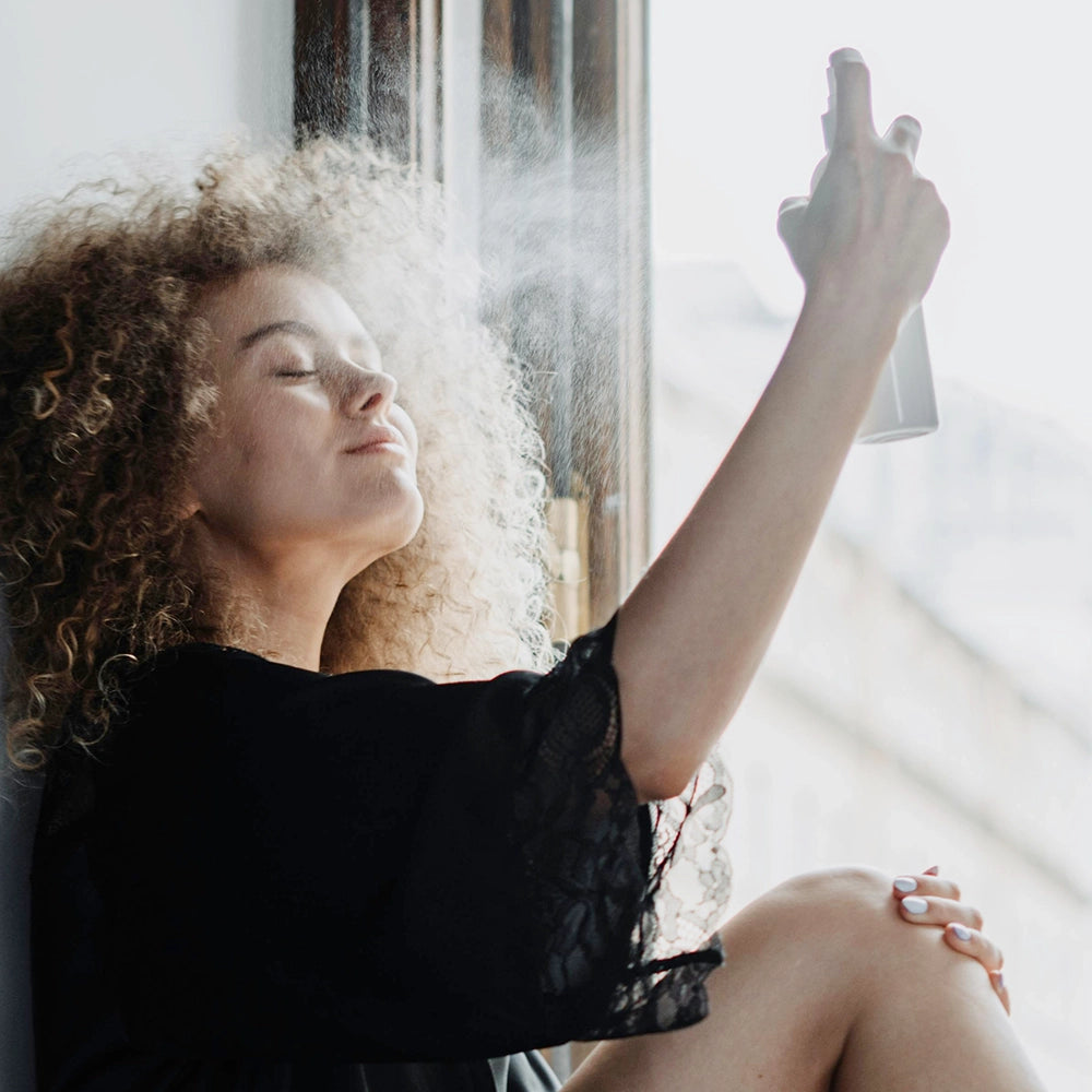 Woman sitting in a window sill spraying a skin product on her face