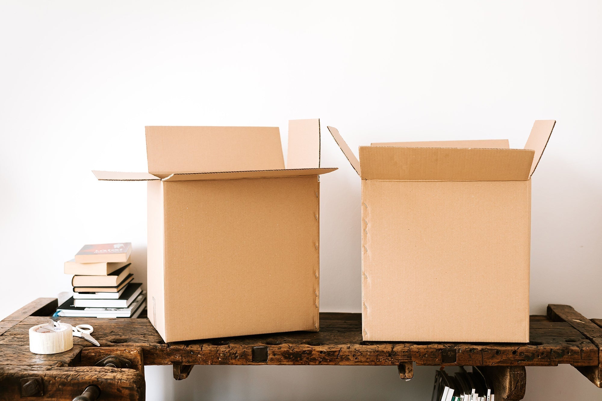 Moving boxes sitting on a wood table with a small stack of books, packing tape and scissors
