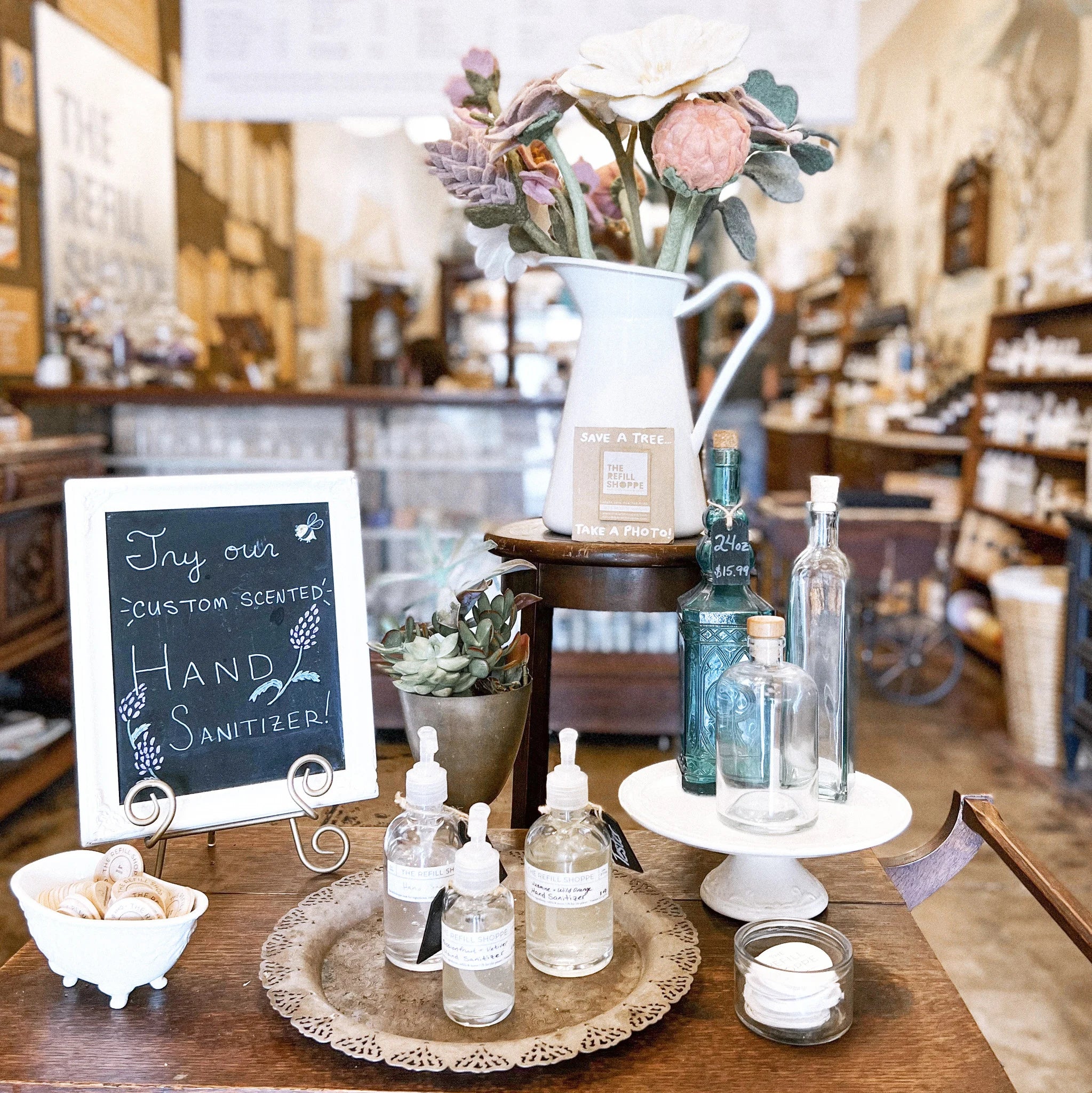 Hand sanitizer bottles on a table with a sign and decorative items and glass bottles in a store setting