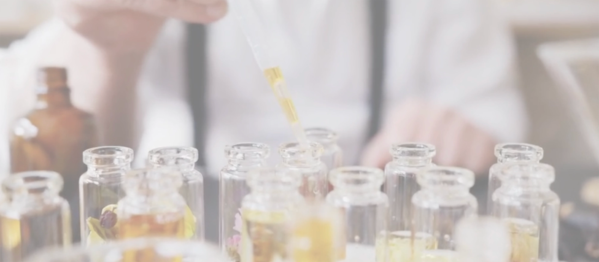 Close-up of small glass vials being filled using a dropper with essential oils against a  blurred background